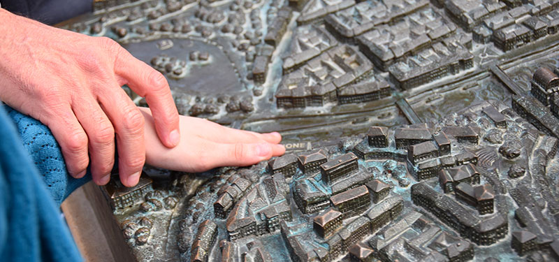Main aidant à découvrir une maquette de la ville lors d'une visite adaptée pour personnes malvoyantes à Lyon